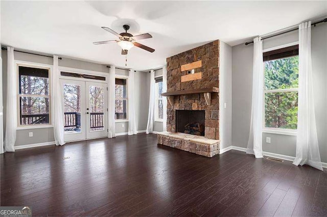 unfurnished living room featuring french doors, ceiling fan, a stone fireplace, wood finished floors, and baseboards