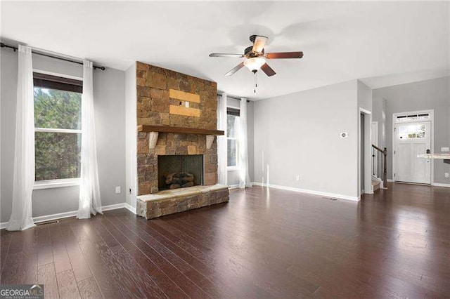 unfurnished living room featuring dark wood-style flooring, a fireplace, a ceiling fan, baseboards, and stairs