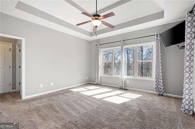 carpeted empty room with a ceiling fan, a raised ceiling, and baseboards