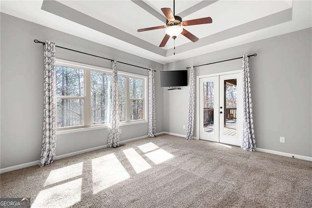 carpeted empty room featuring a ceiling fan, a raised ceiling, baseboards, and french doors