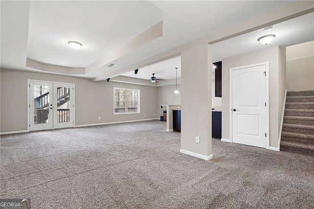 unfurnished living room with stairs, a tray ceiling, carpet, and baseboards