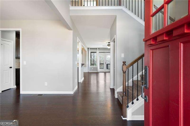 foyer entrance featuring a high ceiling, dark wood-style flooring, a ceiling fan, baseboards, and stairs