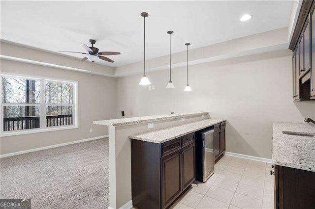 kitchen with light stone counters, a sink, dark brown cabinetry, a peninsula, and baseboards