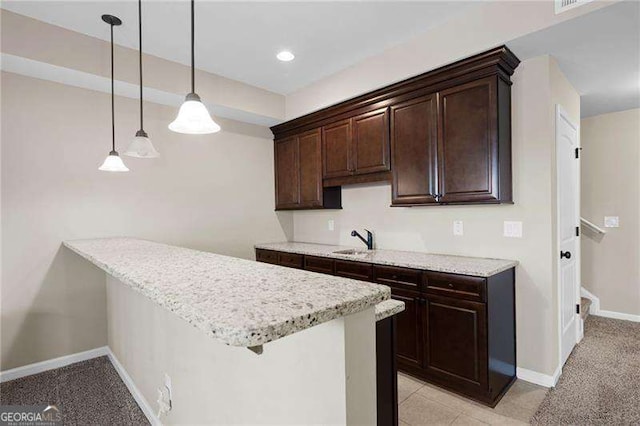 kitchen with dark brown cabinetry, a sink, baseboards, light stone countertops, and decorative light fixtures