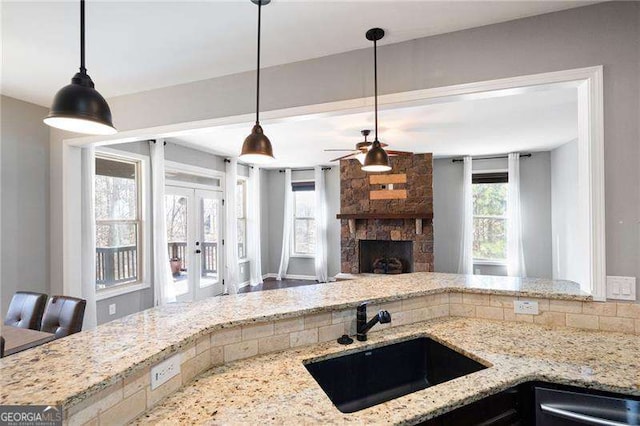 kitchen with a sink, a stone fireplace, stainless steel dishwasher, and light stone countertops