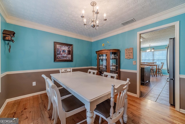 dining space with a textured ceiling, light wood-style floors, visible vents, and a chandelier