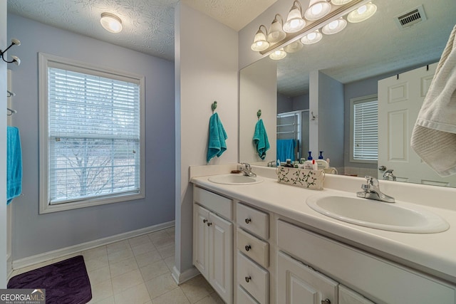 bathroom with a textured ceiling, double vanity, visible vents, and a sink