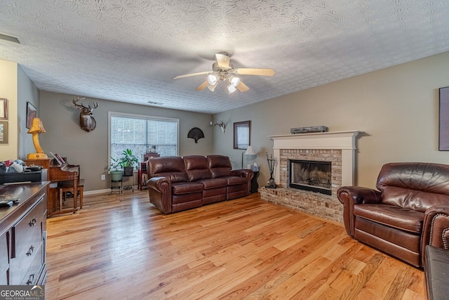 living area featuring a ceiling fan, visible vents, light wood-style flooring, a fireplace, and a textured ceiling