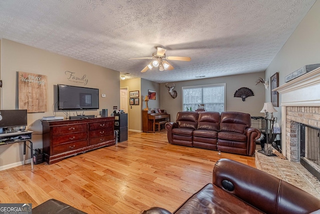 living area with a ceiling fan, wood finished floors, baseboards, a textured ceiling, and a brick fireplace