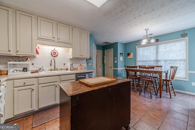 kitchen with a sink, light countertops, dishwasher, cream cabinets, and tasteful backsplash