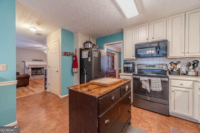 kitchen with a brick fireplace, a kitchen island, light tile patterned floors, decorative backsplash, and appliances with stainless steel finishes