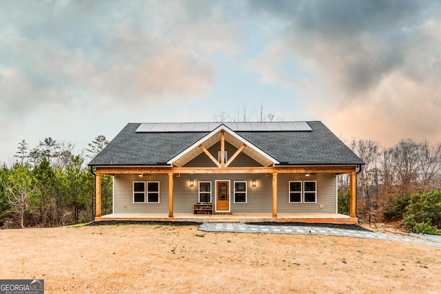 back of property with a porch, roof with shingles, and solar panels