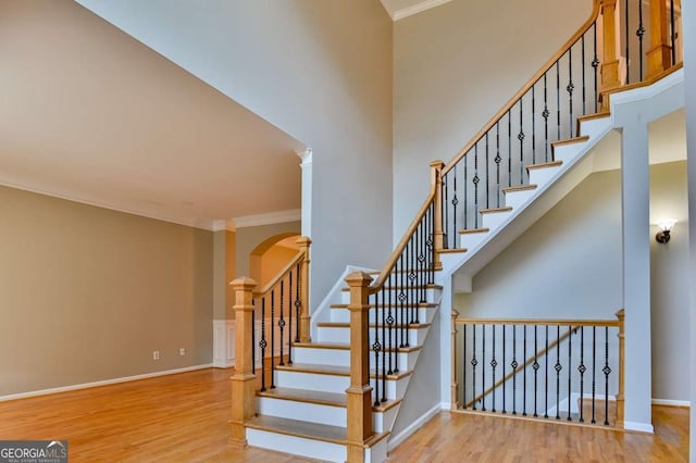 stairway featuring a towering ceiling, wood finished floors, and crown molding