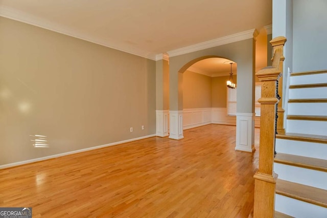 unfurnished room featuring a wainscoted wall, light wood-style flooring, arched walkways, ornamental molding, and stairs