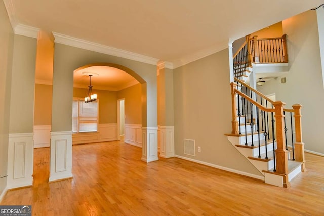 spare room featuring visible vents, a wainscoted wall, wood finished floors, arched walkways, and stairs