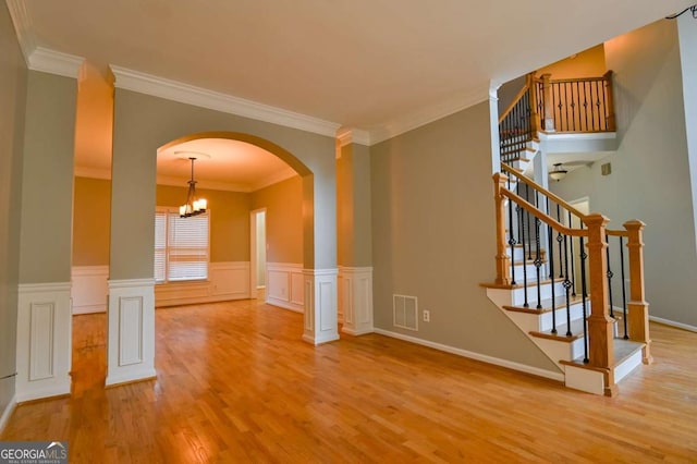 empty room featuring wood finished floors, visible vents, stairs, wainscoting, and a notable chandelier