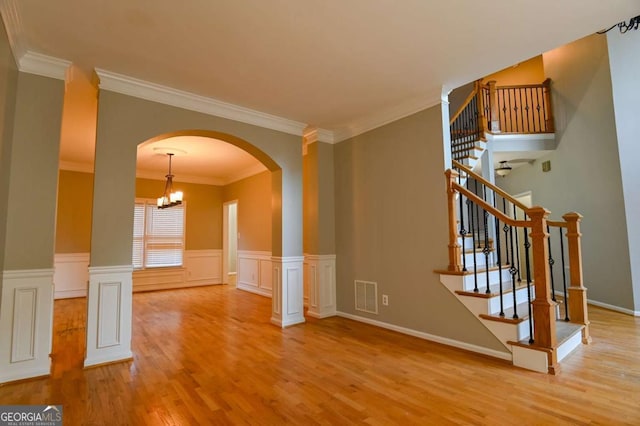 unfurnished room featuring visible vents, stairs, wainscoting, wood finished floors, and arched walkways