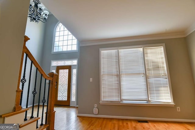 foyer entrance featuring visible vents, crown molding, baseboards, stairway, and wood finished floors