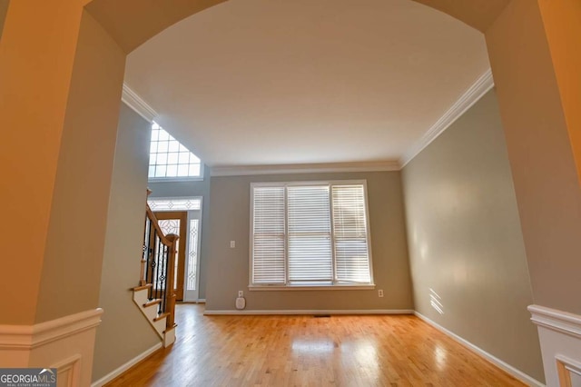 foyer entrance with arched walkways, stairs, crown molding, and wood finished floors