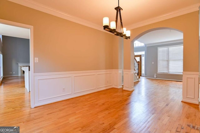 unfurnished dining area with arched walkways, light wood-style floors, an inviting chandelier, crown molding, and stairs