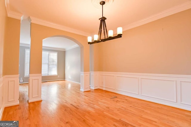 unfurnished dining area featuring a wainscoted wall, arched walkways, ornamental molding, light wood-style floors, and a notable chandelier