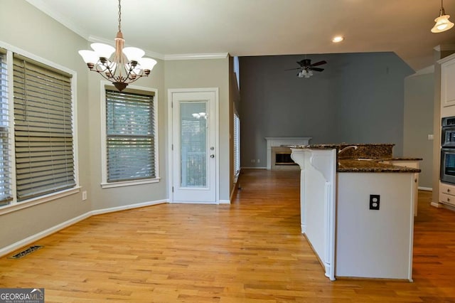 kitchen with light wood finished floors, visible vents, crown molding, ceiling fan with notable chandelier, and white cabinetry