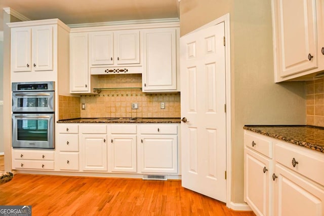 kitchen with dark stone counters, decorative backsplash, light wood-style floors, white cabinets, and stainless steel appliances