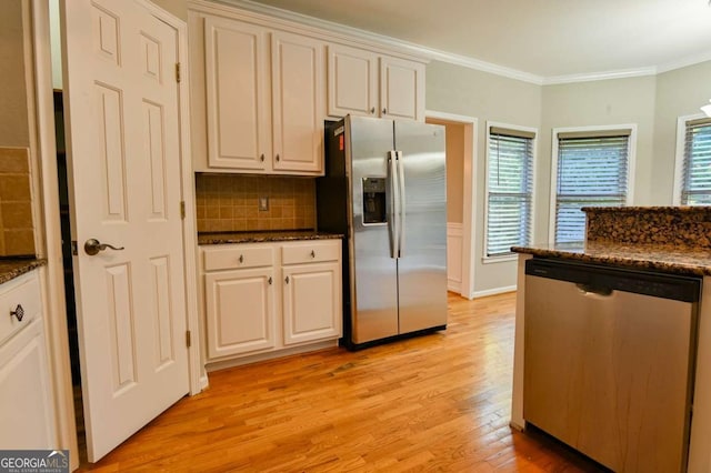 kitchen with ornamental molding, dark stone countertops, light wood-style floors, appliances with stainless steel finishes, and decorative backsplash