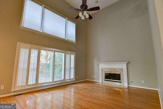 unfurnished living room featuring a tiled fireplace, wood finished floors, visible vents, and baseboards