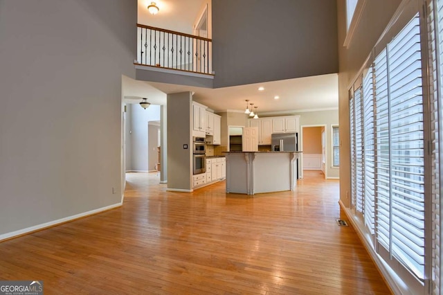 unfurnished living room featuring baseboards, a towering ceiling, crown molding, and light wood finished floors