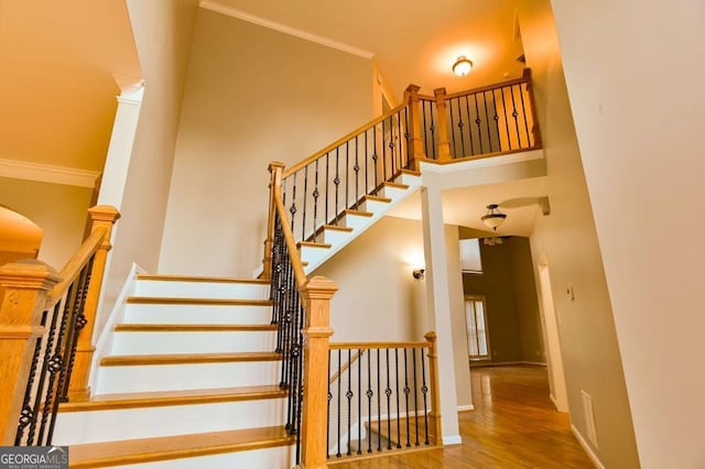 staircase with baseboards, a high ceiling, wood finished floors, and crown molding