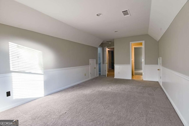 empty room featuring wainscoting, carpet flooring, visible vents, and lofted ceiling