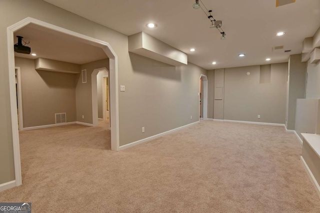 below grade area with visible vents, baseboards, recessed lighting, arched walkways, and light carpet