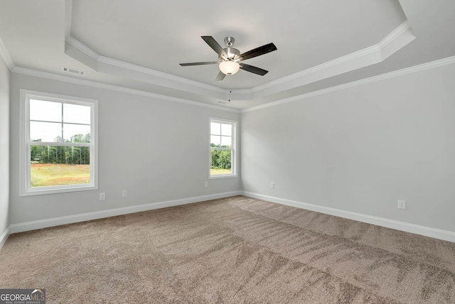 carpeted spare room featuring ornamental molding, a tray ceiling, visible vents, and baseboards