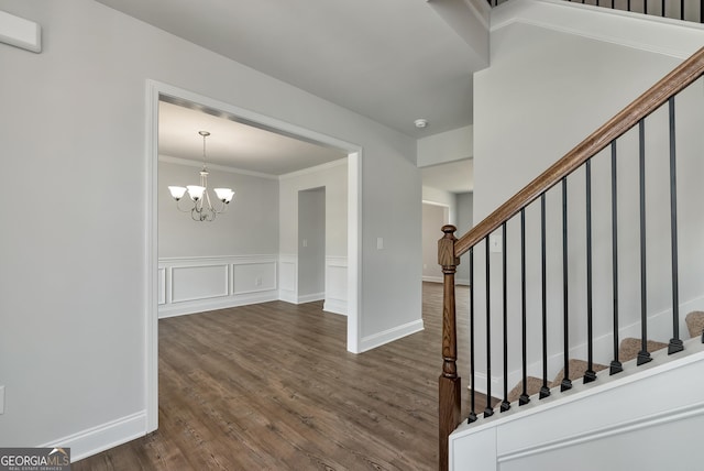 interior space featuring stairs, ornamental molding, wainscoting, dark wood-style floors, and an inviting chandelier