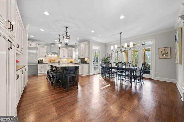 kitchen with a breakfast bar area, a kitchen island, a chandelier, stainless steel built in refrigerator, and wall chimney exhaust hood