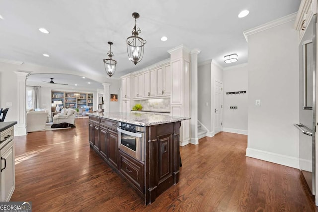 kitchen with dark brown cabinetry, appliances with stainless steel finishes, dark wood-style flooring, crown molding, and ornate columns