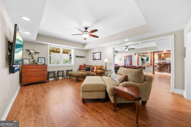 living area with a raised ceiling, baseboards, and wood finished floors