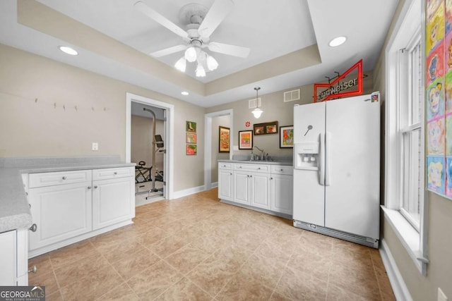 kitchen featuring a tray ceiling, white refrigerator with ice dispenser, recessed lighting, white cabinets, and a sink