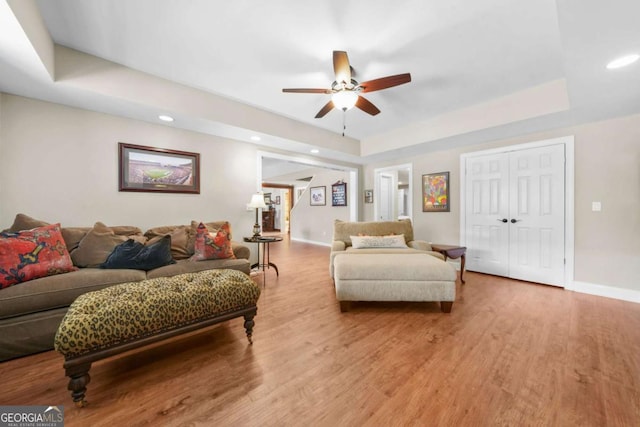 living area featuring light wood-style floors, a raised ceiling, baseboards, and a ceiling fan