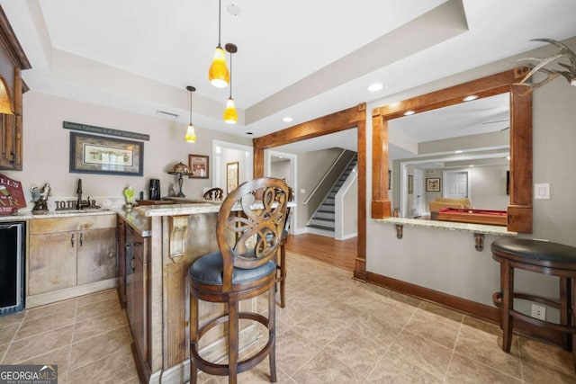 kitchen with a peninsula, a sink, baseboards, a raised ceiling, and a kitchen bar