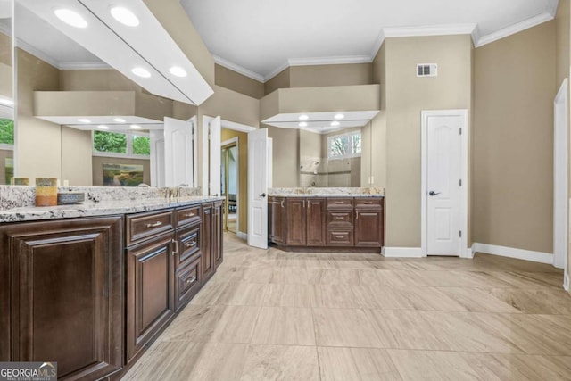 kitchen with dark brown cabinetry, baseboards, visible vents, and crown molding