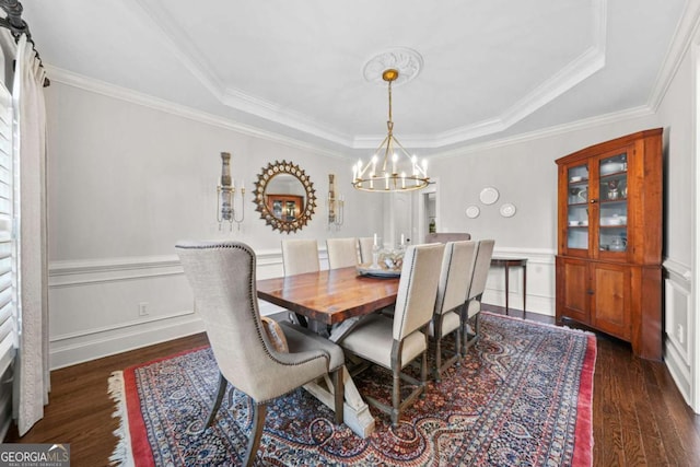 dining area featuring a chandelier, a decorative wall, wainscoting, a tray ceiling, and dark wood finished floors