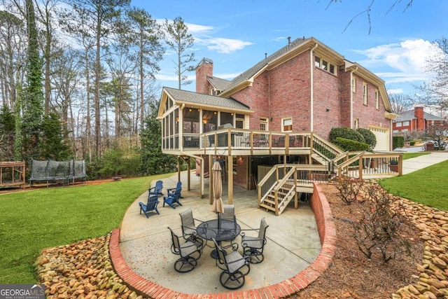 back of house featuring a trampoline, a chimney, a lawn, a sunroom, and a patio area