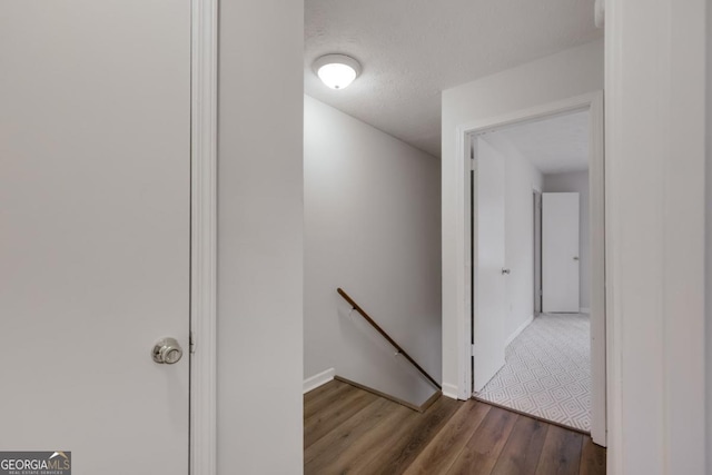 hallway featuring a textured ceiling, baseboards, wood finished floors, and an upstairs landing