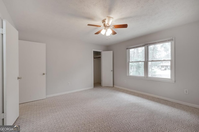 unfurnished bedroom with a textured ceiling, light colored carpet, a ceiling fan, and baseboards