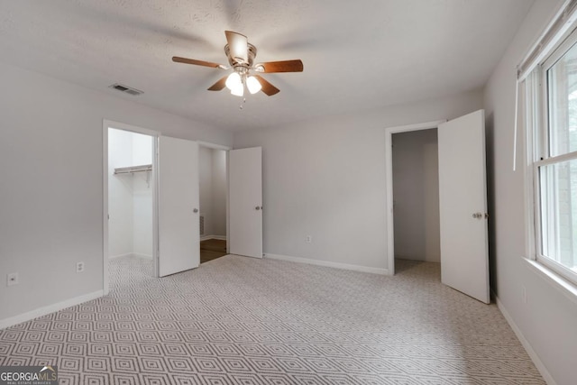 unfurnished bedroom with baseboards, visible vents, a walk in closet, and a ceiling fan