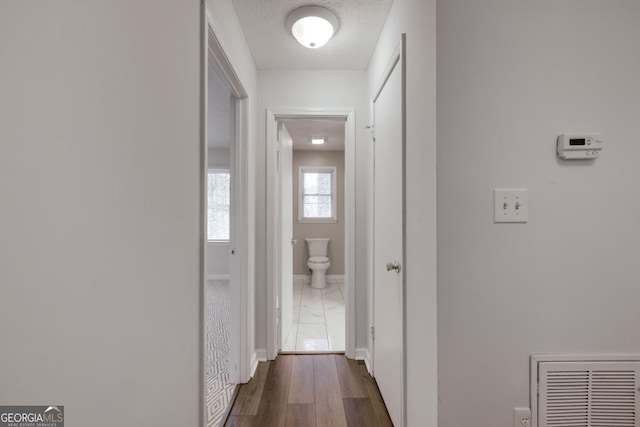 hallway featuring dark wood-type flooring, visible vents, and baseboards