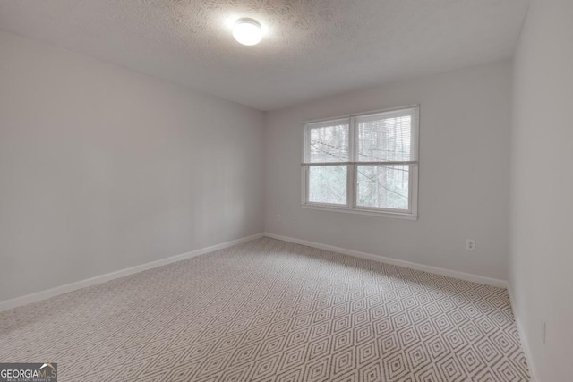 empty room featuring light colored carpet, a textured ceiling, and baseboards