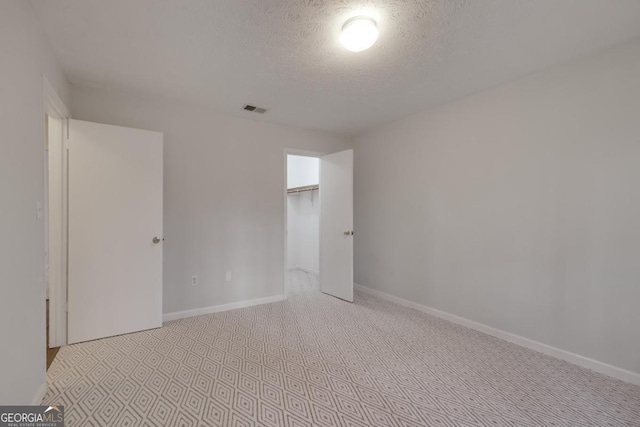 unfurnished bedroom featuring a closet, visible vents, a spacious closet, a textured ceiling, and baseboards